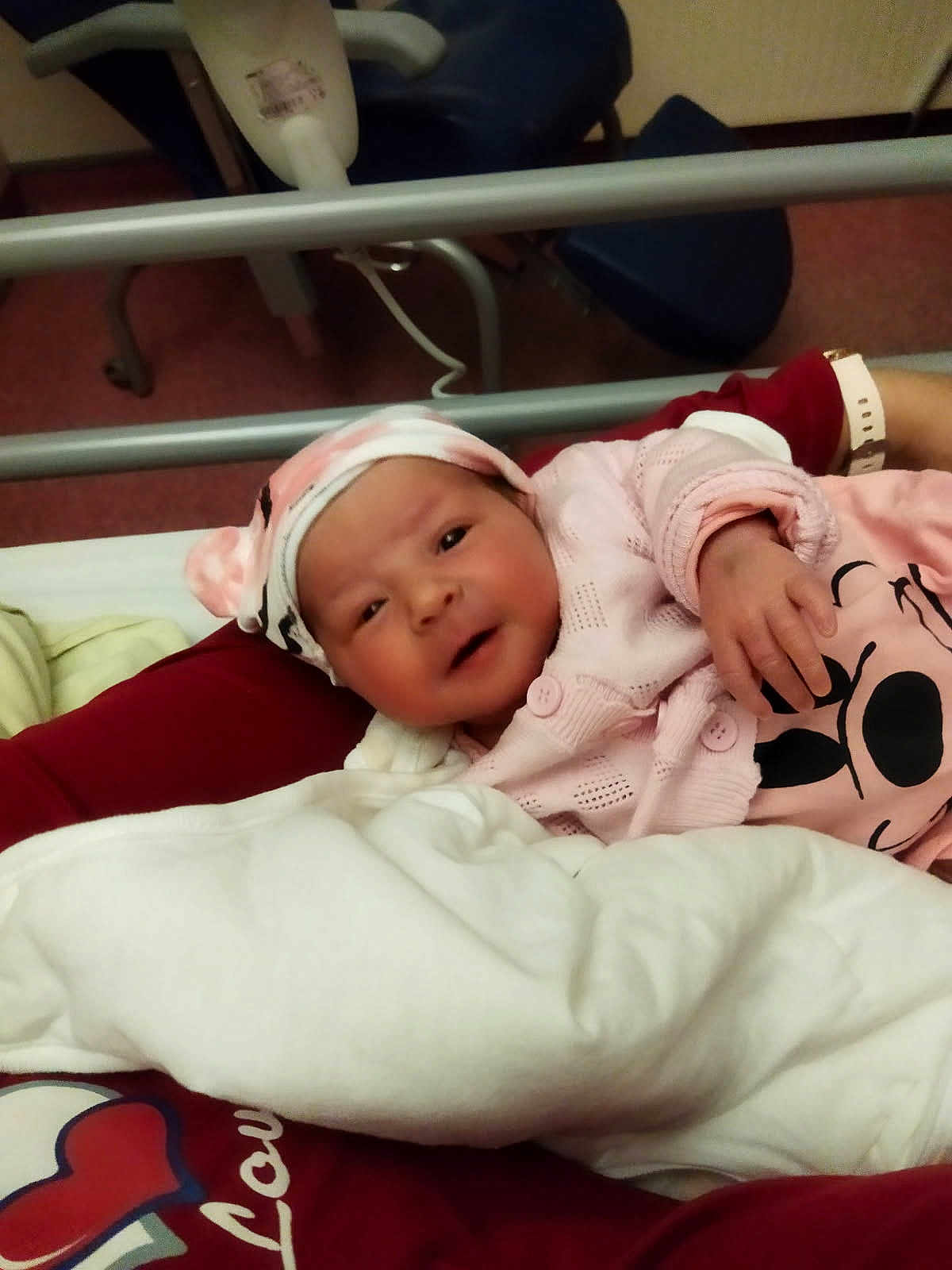 Iyana a rejoint le concours — aidez-le/la à gagner de superbes lots ! newborn, baby, infant, hospital_bed, person, pink_clothing, hat, blanket, arm, hospital_equipment, chair, indoor, bed, face, cute, lying_down, holding, smile, human, resting