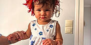 Ohaina participe au concours pour gagner de l'argent avec cette photo : child, toddler, flower_crown, white_dress, blue_flowers, indoor, holding_hands, adult_hands, curly_hair, serious_expression, beads, wall, light_switch, person, portrait, standing, skin, watch, bracelet, home