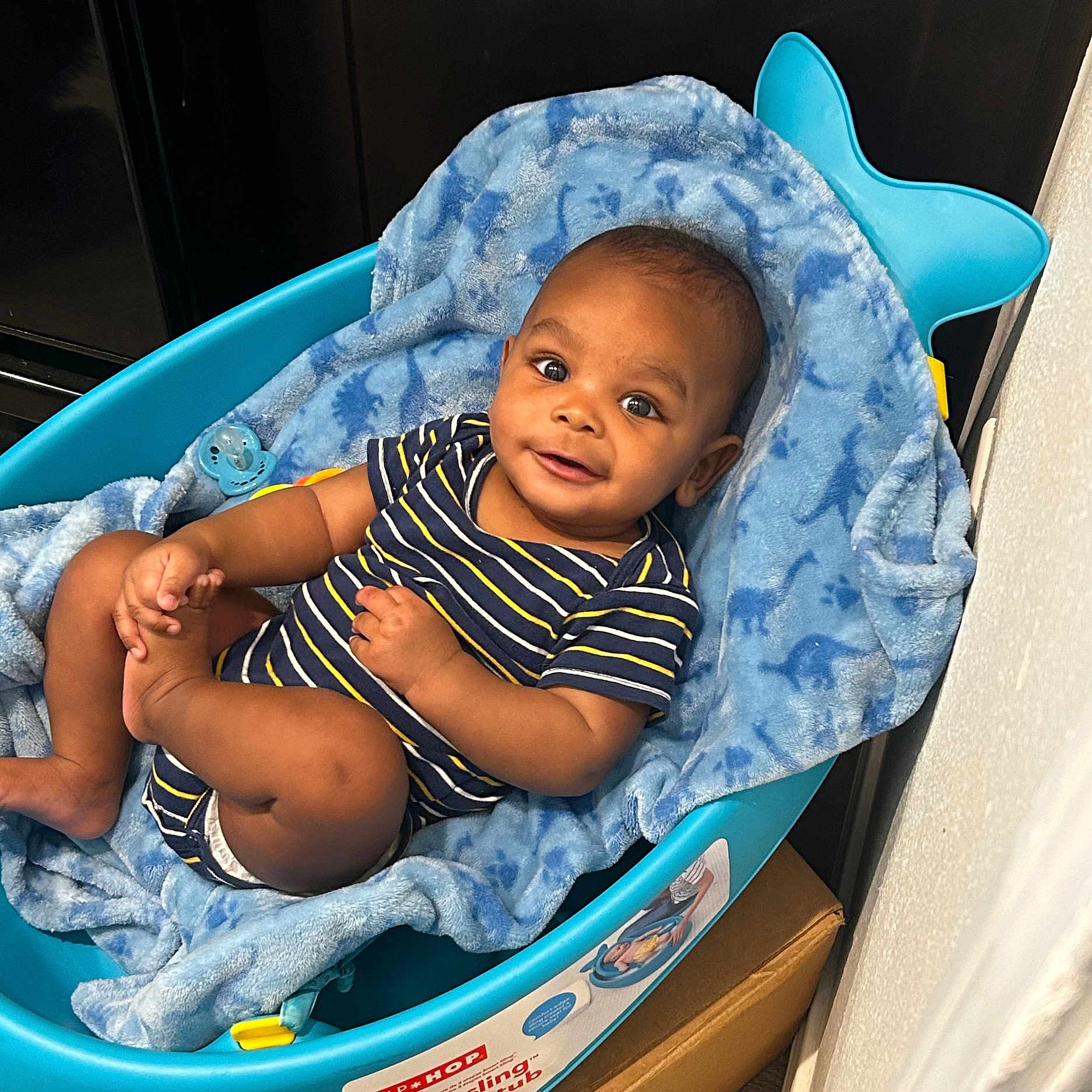 Darius Jr is registered to the contest to win money with this photo: baby, infant, blue, blanket, baby_tub, striped_clothing, smiling, happy, cute, child, indoors, playful, onesie, foot, hand, face, eyes, head, skin, relaxing