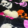 kitten, cat, sleeping, white_fur, fluffy, blanket, colorful, skull_pattern, orange, pink, black, cozy, soft_texture, cute, small, resting, animal, pet, indoors, furry