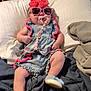 accessory, baby, bed, blanket, blue_shoes, bow, casual, child, cute, denim_dress, fashion, indoor, infant, pacifier, person, pillow, pink, relaxing, resting, sunglasses