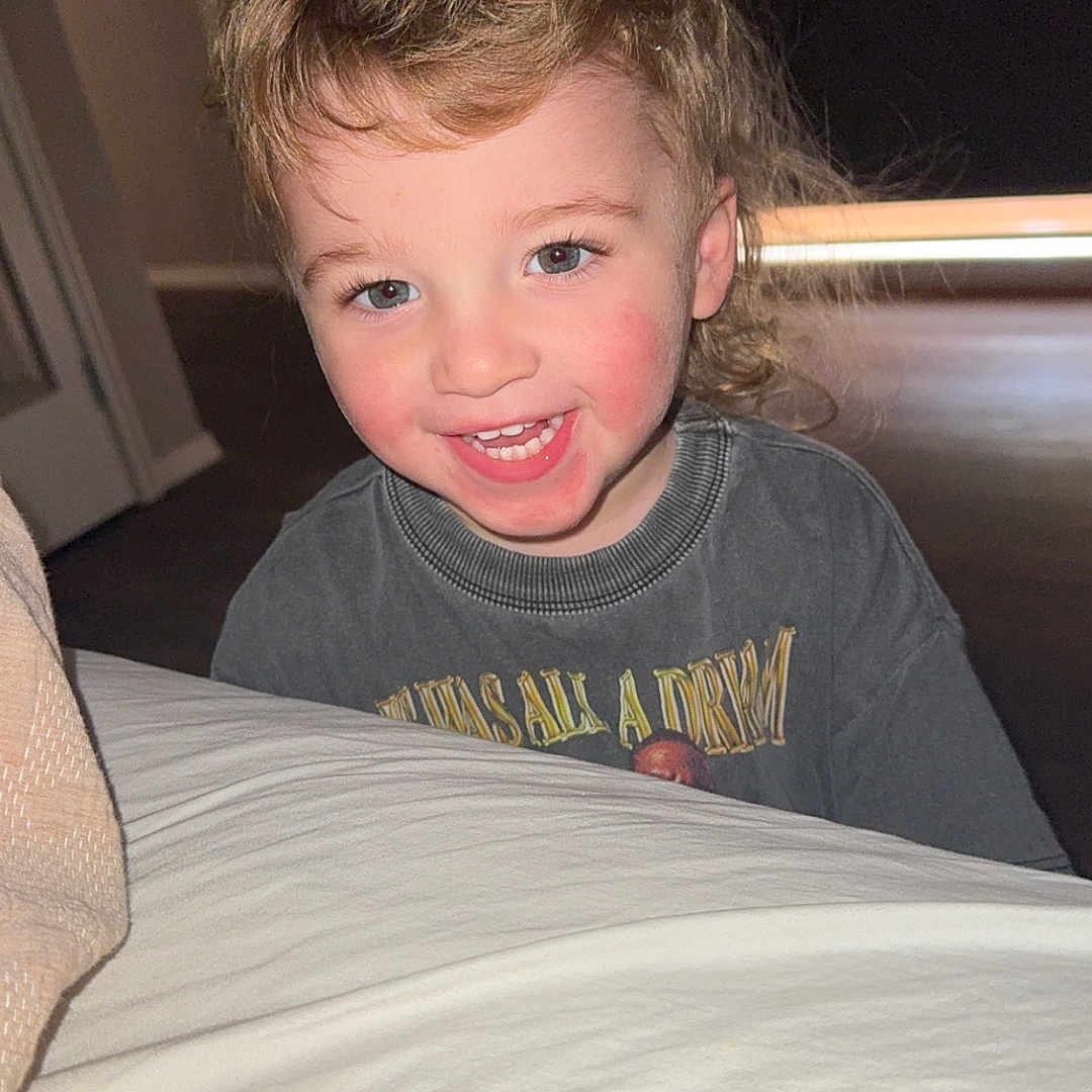 Noah is registered to the contest to win money with this photo: background, child, clothing, cute, expression, eyes, face, hair, happy, head, indoor, light, mouth, person, portrait, rosy_cheeks, skin, smiling, tshirt, young