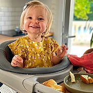 Rose participe au concours pour gagner de l'argent avec cette photo : toddler, child, high_chair, smile, bread, plate, kitchen, window, flower_pattern, hair_clip, yellow_dress, table, food, indoor, happy, person, young_child, face, seat, daylight