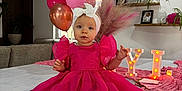 Lyla a rejoint le concours — aidez-le/la à gagner de superbes lots ! toddler, pink_dress, headband, balloons, birthday, table, marquee_letters, decorations, pink_theme, living_room, couch, plants, photos, celebration, party, fabric, indoor, child, smiling, festive