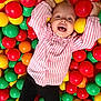child, toddler, ball_pit, plastic_balls, colorful, pink_shirt, black_pants, happy, smiling, play, fun, indoor, leisure, joyful, cute, childhood, recreation, casual_clothing, entertainment, playtime