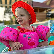 Lyla a rejoint le concours — aidez-le/la à gagner de superbes lots ! child, toddler, pool, floaties, red_hat, pink, flamingo, summer, water_toy, toy_dolphin, smiling, outdoor, sunny, swimming, swimwear, play, happy, baby, necklace, canopy