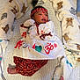 newborn, baby, infant, blanket, headband, peacock_feather, red_clothing, white_clothing, patterned_clothing, cushion, plush_toy, animal_print, bed, lying_down, indoors, portrait, cute, soft_texture, decorative, peaceful