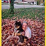 person, dog, autumn_leaves, grass, suburban, house, smiling, outdoor, fall, leaf_pile, pet, casual, candid, leaves, nature, daytime, happy, embrace, animal, yard