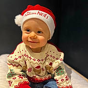 Sacha participe au concours pour gagner de l'argent avec cette photo : baby, child, smiling, santa_hat, christmas_sweater, festive, holiday, cute, portrait, indoor, clothing, jeans, happy, person, infant, face, headwear, seated, soft_surface, dark_background