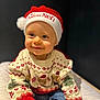 baby, child, smiling, santa_hat, christmas_sweater, festive, holiday, cute, portrait, indoor, clothing, jeans, happy, person, infant, face, headwear, seated, soft_surface, dark_background