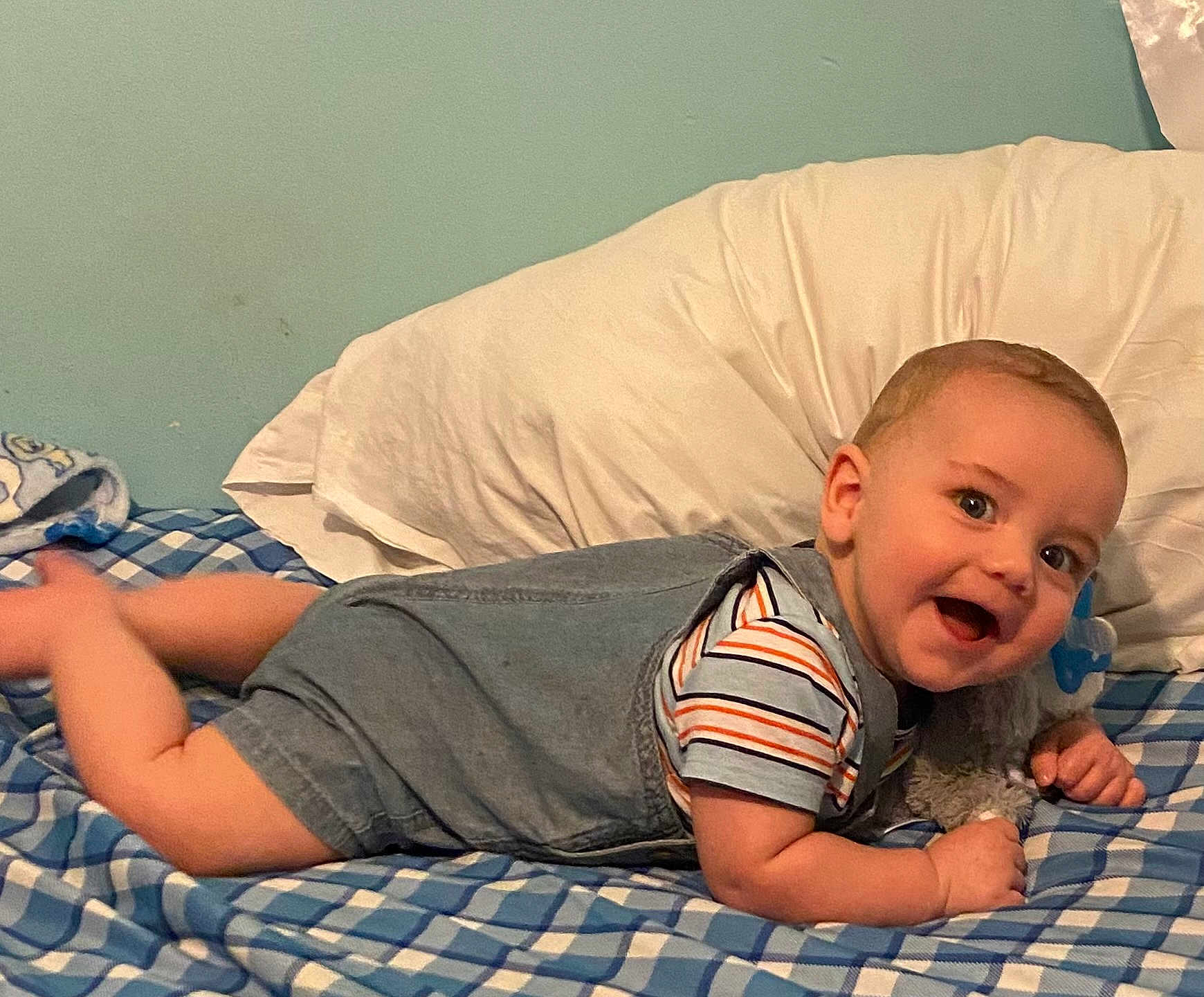 Brayden joined the competition — help win amazing prizes! baby, child, smiling, bed, pillow, denim_overalls, striped_shirt, blue_checkered_bedspread, happy, indoor, face, person, cute, skin, head, eyes, mouth, furniture, resting, lying_down