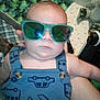 Brayden is registered to the contest to win money with this photo: baby, child, sunglasses, blue_clothing, romper, indoor, person, face, head, hand, patterned_clothing, toy, bed, blanket, plush, infant, cute, casual, young_child, holding