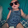 baby, sunglasses, blue_romper, airplane_print, helicopter_print, cushion, plaid_blanket, infant, child, clothing, indoor, blur, pose, cute, cool, relaxing, person, headwear, legs, soft_toy
