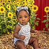 Azianna is registered to the contest to win money with this photo: toddler, child, sunflowers, headband, bow, outdoor, nature, flowers, plants, wood_chips, red_wall, summer, cute, baby, sitting, portrait, greenery, sunlight, curious, garden