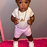 toddler, child, girl, standing, pink_bow, gold_chain, white_shirt, pink_shorts, sneakers, pink_rug, indoor, cute, fashion, jewelry, portrait, young_child, footwear, happy, expressive_eyes, casual_clothing