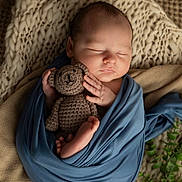 Kolter joined the competition — help win amazing prizes! newborn, baby, sleeping, wrapped, blue_cloth, crocheted_teddy_bear, blanket, knit, cozy, soft, peaceful, infant, cute, hand, foot, plant, greenery, portrait, indoors, rest