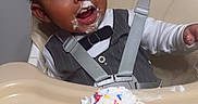 Kiyear is registered to the contest to win money with this photo: toddler, child, high_chair, cupcake, frosting, sprinkles, food, happy, messy, face, clothing, white_shirt, gray_vest, indoor, person, celebration, cute, smile, baby_food, feeding