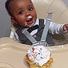 toddler, child, high_chair, cupcake, frosting, sprinkles, food, happy, messy, face, clothing, white_shirt, gray_vest, indoor, person, celebration, cute, smile, baby_food, feeding