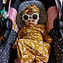 baby, car_seat, sunglasses, flower_shaped, headwrap, yellow_outfit, floral_pattern, infant, child, seatbelt, indoor, cute, fashion, accessory, person, portrait, clothing, baby_clothes, baby_accessory, seat