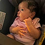 baby, infant, car_seat, pink_onesie, child, face, hand, looking_sideways, curious, seatbelt, indoors, soft_light, portrait, young_child, newborn, clothing, seat, captive, sitting, person