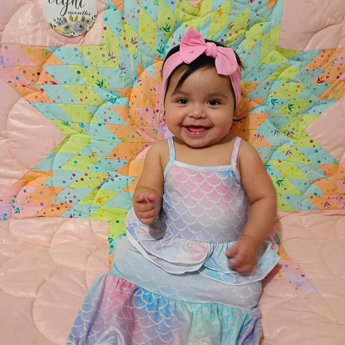 Wahcá is registered to the contest to win money with this photo: baby, celebration, child, colorful, cute, dress, eight_months, fabric, happy, headband, indoors, infant, milestone, pastel_colors, patterned_quilt, pink_bow, portrait, quilt, sitting, smiling