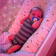 Harrison is registered to the contest to win money with this photo: baby, baby_bed, blanket, child, comfort, cozy, cute, dinosaur_pattern, indoors, infant, mesh_sides, newborn, onesie, pacifier, pink_light, resting, sleeping_area, small_baby, soft_texture, striped_clothing