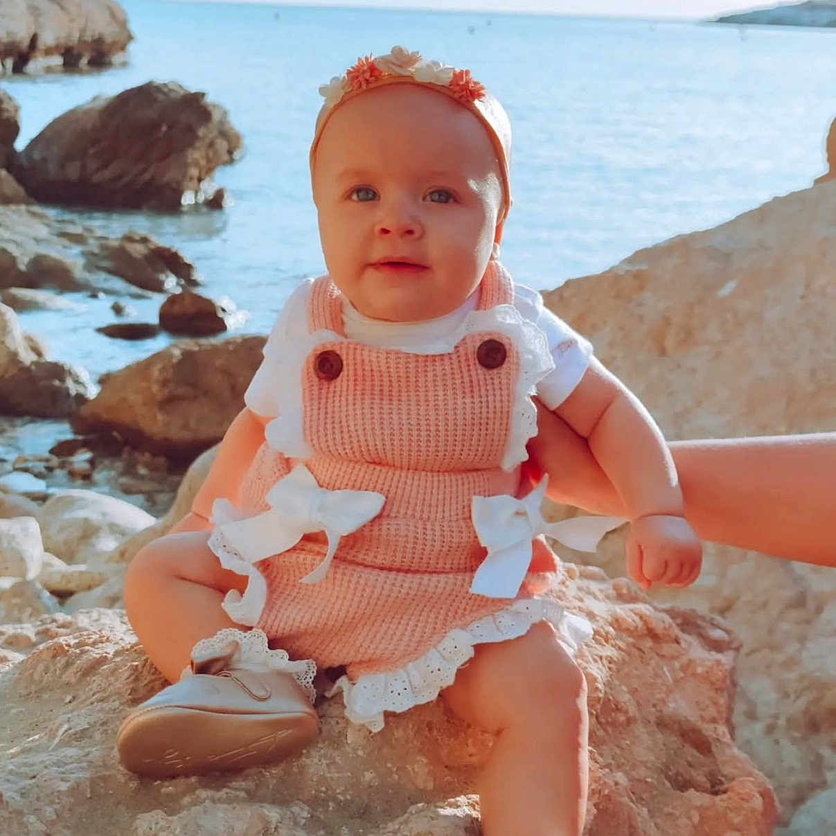 Luna Ariana a rejoint le concours — aidez-le/la à gagner de superbes lots ! baby, blue_sky, child, clothing, cute, footwear, hand, happy, headband, infant, nature, outdoor, person, portrait, rock, sea, sitting, summer, sunlight, water