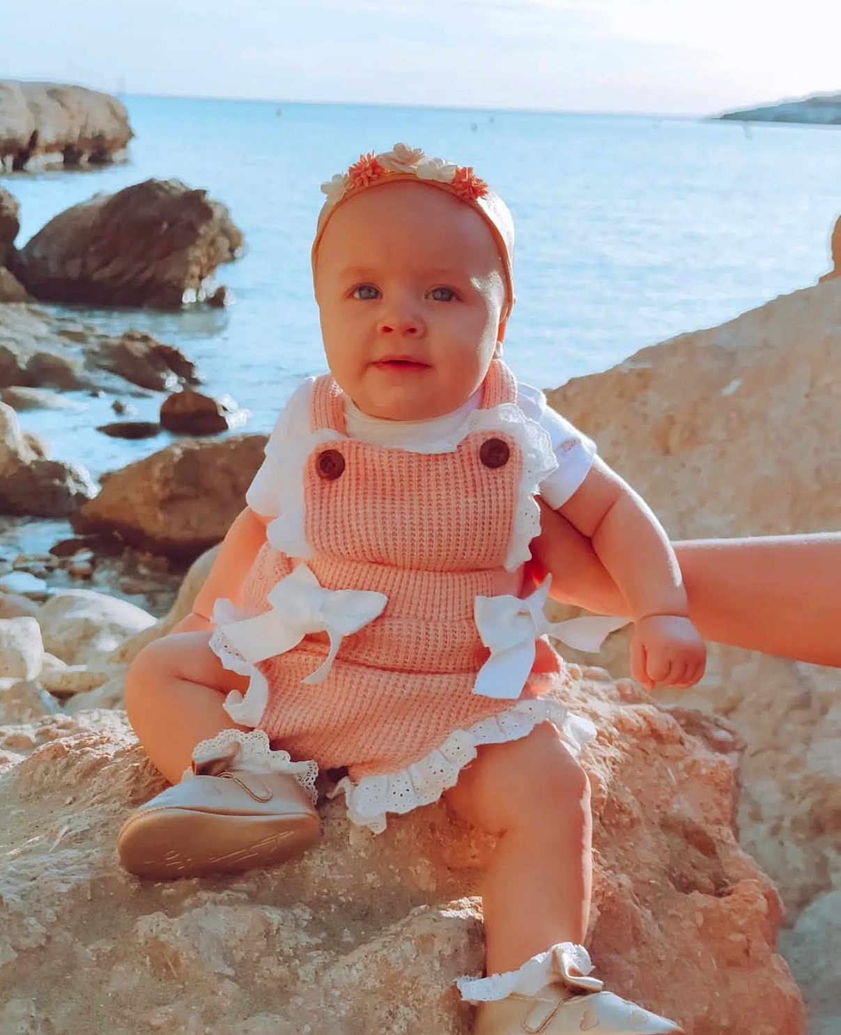 Luna Ariana a rejoint le concours — aidez-le/la à gagner de superbes lots ! baby, child, rock, sea, water, outdoor, nature, hand, clothing, headband, footwear, sunlight, summer, cute, portrait, sitting, person, infant, happy, blue_sky