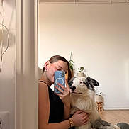 Fuego participe au concours pour gagner de l'argent avec cette photo : person, dog, mirror, selfie, floor, casual_clothing, plant, minimalist, home_interior, wooden_floor, black_top, jeans, pet, cute, relaxed, indoor, technology, smartphone, reflection, seated