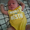 baby, infant, yellow_onesie, text_on_clothing, blanket, patterned_blanket, lying_down, arms_outstretched, cute, child, young_baby, clothing, soft_fabric, indoors, resting, newborn, human, person, casual, relaxed