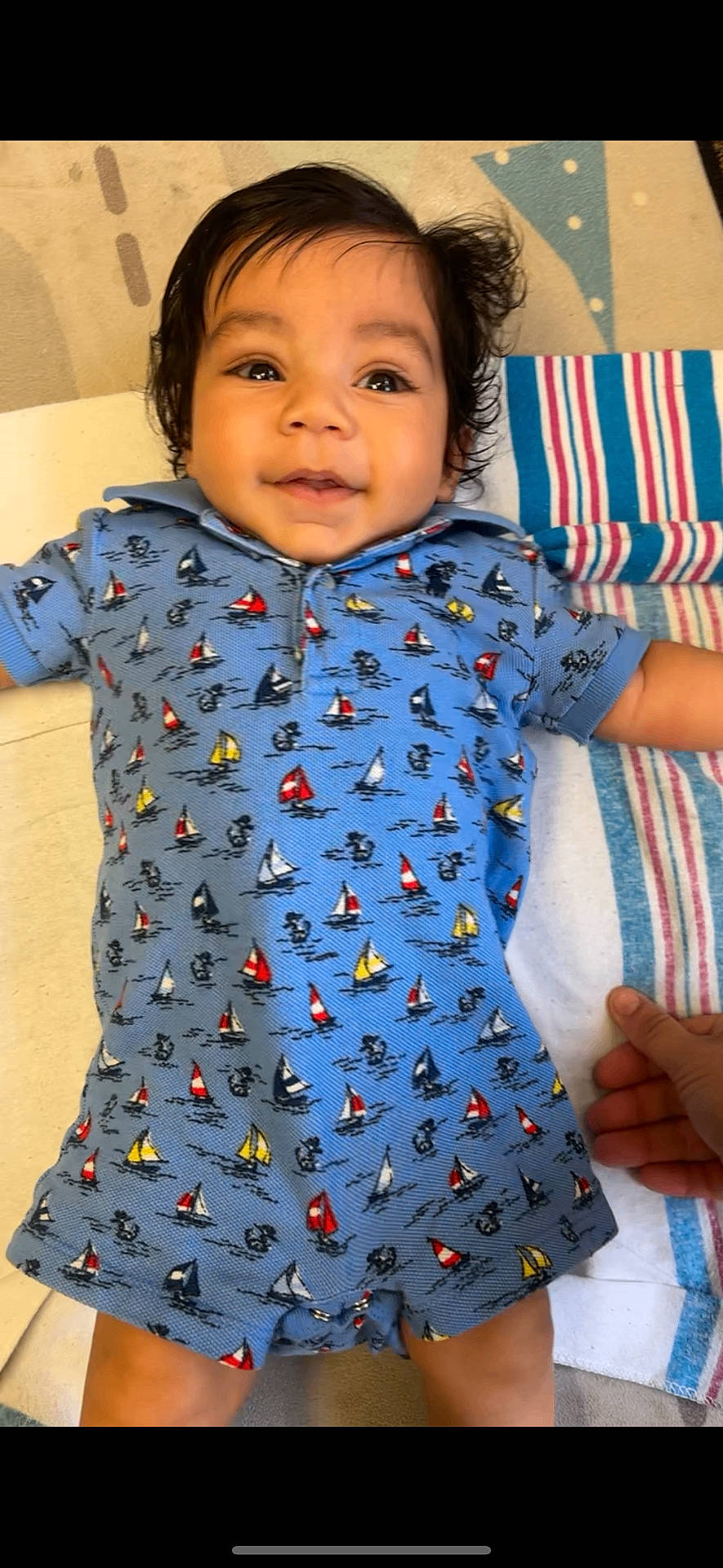 Tairell joined the competition — help win amazing prizes! baby, blue_onesie, child, clothing, cute, fabric, face, hair, hand, happy, indoors, infant, lying_down, person, portrait, sailboat_pattern, skin, smiling, striped_towel, toddler