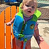 Laura is registered to the contest to win money with this photo: toddler, child, life_jacket, orange_chair, outdoor, wet_hair, curly_hair, pool_area, fence, sunny, shadow, concrete, purple_shirt, red_ankle_band, person, baby, summer, water_safety, daylight, playful