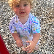 Laura is registered to the contest to win money with this photo: toddler, child, blonde_hair, curly_hair, blue_eyes, shirt, colorful_clothing, rainbow, flower_pattern, outdoor, playground, wood_chips, hands, standing, looking_up, casual, daylight, expression, cute, young_child