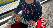 Laura joined the competition — help win amazing prizes! toddler, child, curly_hair, sitting, red_stool, colorful_clothing, heart_pattern, navy_blue_top, indoor, mesh_screen, banner, playful, floor_carpet, cute, portrait, baby, young_child, casual, smiling, person
