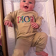 Ava is registered to the contest to win money with this photo: baby, infant, child, smiling, dior, clothing, beige_outfit, cushion, changing_pad, wooden_frame, playful, happy, face, foot, hand, stars_pattern, elephant_illustration, bear_illustration, indoors, person