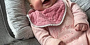 Ava is registered to the contest to win money with this photo: baby, infant, smiling, pink_clothing, bib, baby_seat, gray, cushion, happy, cute, portrait, child, small_hands, cozy, indoors, soft_fabric, newborn, face, joy, relaxed