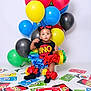 toddler, child, balloons, uno_cards, colorful, party, costume, black_socks, red_bows, studio, playful, celebration, game, cute, portrait, smiling, sitting, indoors, bright, fun