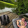 Winter is registered to the contest to win money with this photo: baby, baby_seat, stuffed_animal, fishing_rod, backpack, dock, lake, water, trees, greenery, outdoor, nature, wood, smiling, infant, relaxing, summer, candid, child, happy