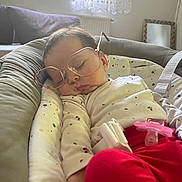 Sare-Nour participe au concours pour gagner de l'argent avec cette photo : baby, baby_seat, blanket, child, couch, face, glasses, hand, indoors, infant, natural_light, pacifier, patterned_clothing, peaceful, red_pants, resting, sleeping, soft_furniture, white_clothing, window