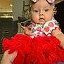 baby, child, blue_eyes, bow, red_skirt, tutu, strawberry_pattern, cute, indoor, person, infant, clothing, sitting, couch, hand, face, portrait, headband, pink, adorable