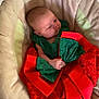 baby, infant, child, dress, red_bow, lace, green_clothing, cushion, seat, soft_fabric, indoor, portrait, cute, small_hands, head, face, looking_sideways, comfortable, resting, newborn