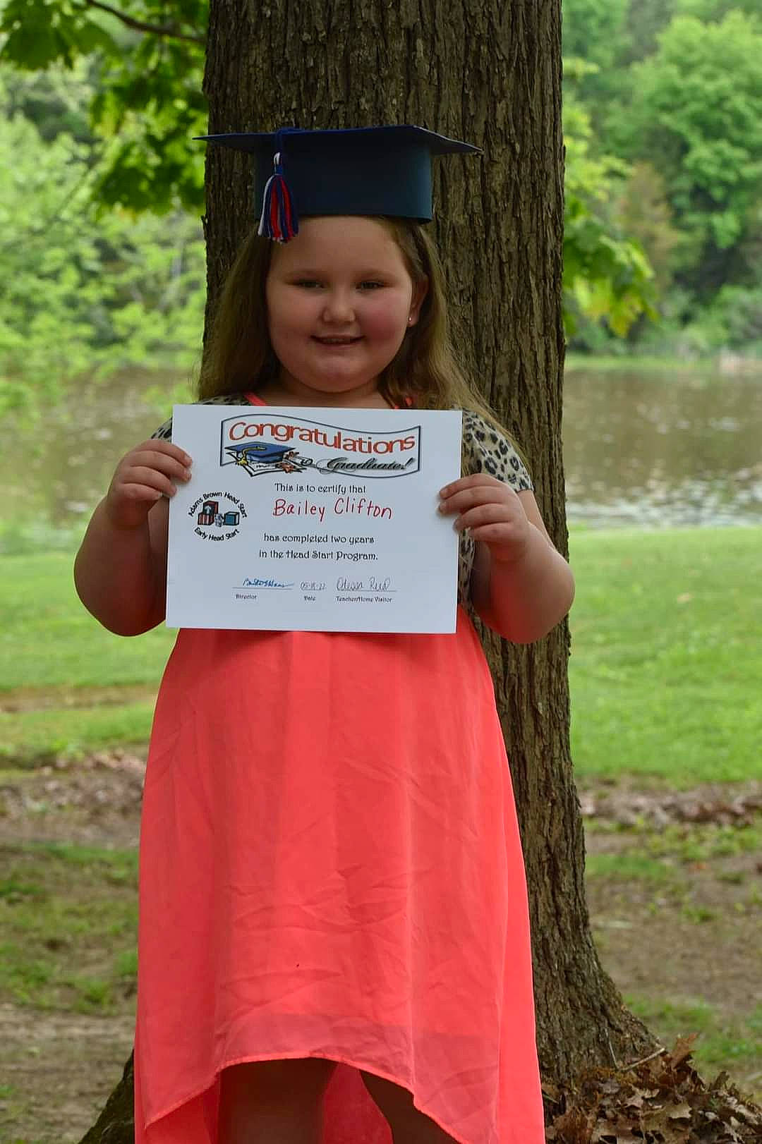 Bailey is registered to the contest to win money with this photo: academic_dress, child, dress, event, eye, fun, graduation, grass, hand, happy, headwear, joy, leisure, mortarboard, nature, people_in_nature, person, plant, scholar, skin