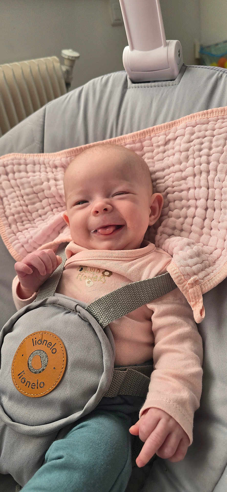 Lucie a rejoint le concours — aidez-le/la à gagner de superbes lots ! baby, infant, smiling, drooling, pink_blanket, baby_bouncer, safety_harness, onesie, face, hand, leg, ear, soft_texture, plush, cozy, portrait, home_interior, radiator, brand_label, gray_fabric