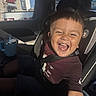 child, toddler, car_seat, car_interior, smiling, happy, seatbelt, short_hair, casual_clothing, sunlight, window, drink_container, blue, seat, person, portrait, daylight, vehicle, joy, candid