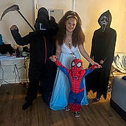 Kristopher joined the competition — help win amazing prizes! child, costume, spiderman, ghost_mask, scythe, dress, indoor, floor, smile, person, group, holding_hands, headband, footwear, wood_floor, door, furniture, black_clothing, white_dress, mask