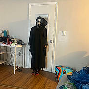 Shayla is registered to the contest to win money with this photo: person, costume, mask, ghostface, door, mirror, reflection, table, clutter, water_bottle, floor, wood_floor, shopping_bag, aldi, couch, blanket, snack_bag, room, indoor, lighting