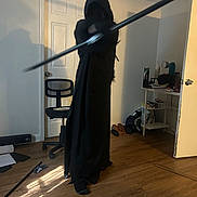Nicholas joined the competition — help win amazing prizes! person, hood, black_clothing, staff, indoors, wood_floor, chair, door, shoes, socks, desk, bag, papers, shadow, light, mystery, pose, floor, object, room