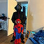 child, costume, spiderman, indoor, person, floor, door, room, adult, hand, black_clothing, red, blue, sneakers, blanket, couch, bag, wood_floor, curtain, wall