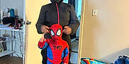 Maeson is registered to the contest to win money with this photo: child, costume, spiderman, adult, black_clothing, hood, indoor, door, floor, wooden_floor, bag, blanket, furniture, person, pose, curtain, room, socks, toy_shoes, light_switch