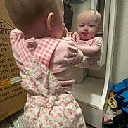 Lilly joined the competition — help win amazing prizes! baby, mirror, reflection, clothing, pink, overalls, standing, tongue_out, carpet, box, room, furniture, child, curious, indoor, person, baby_girl, playful, face, expression